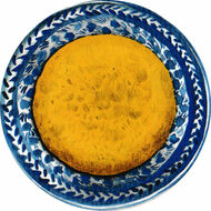 A round, golden-yellow tortilla on a decorative blue and white plate with intricate patterns